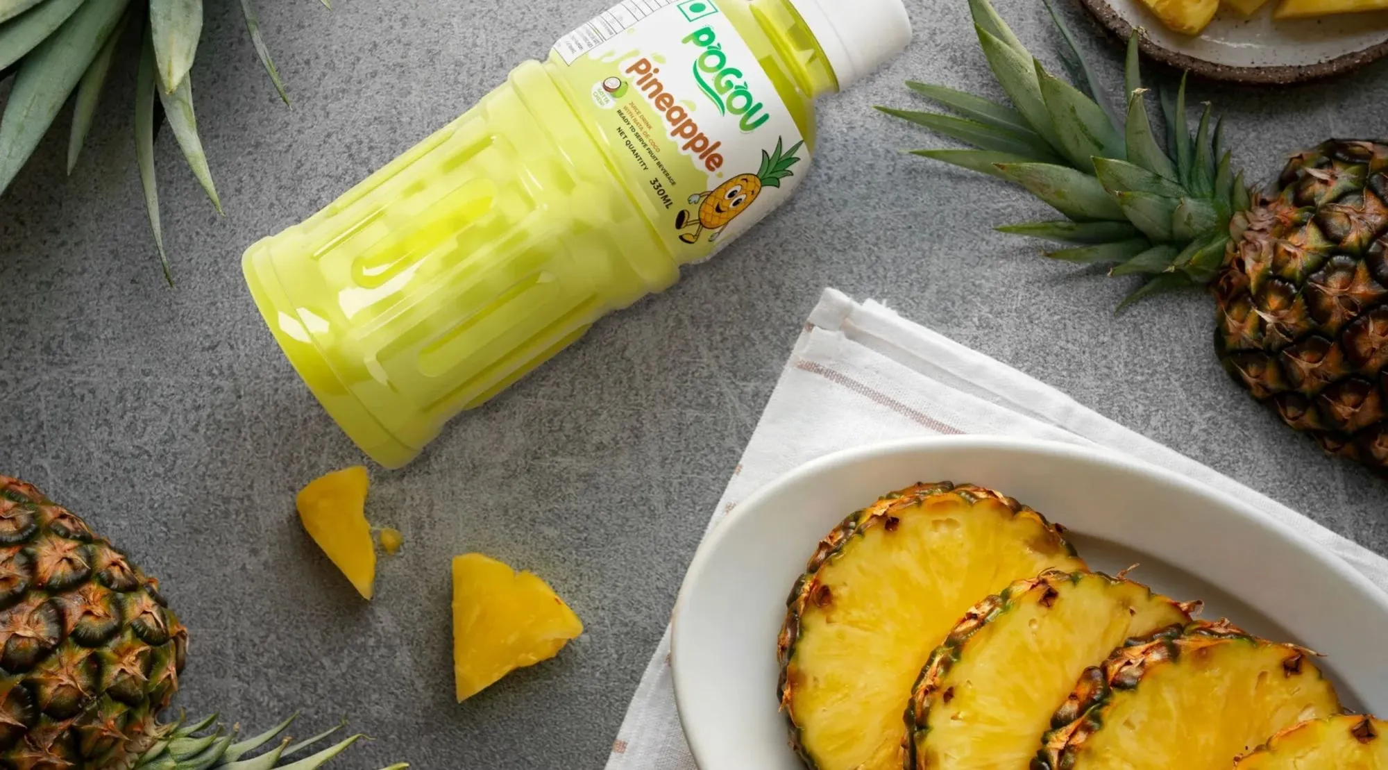 A bottle of Pogou Pineapple juice lying beside pineapple slices